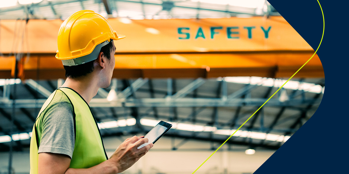 A construction worker in a yellow helmet and reflective vest attentively reads a tablet with 'SAFETY' prominently displayed in the background, emphasizing field service safety workflows.